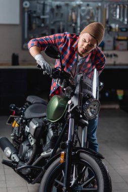 mechanic in checkered shirt and gloves examining brake handle on motorbike handlebar clipart