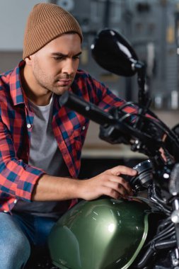 Ekose gömlekli ve bereli genç tamirci atölyede motosiklet kontrolü yapıyor.