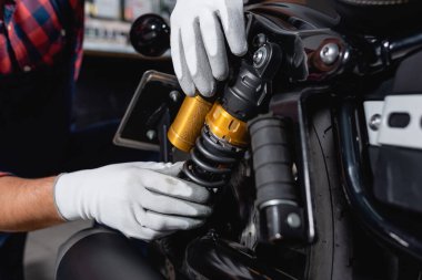 cropped view of mechanic checking shock absorber of motorcycle in workshop clipart