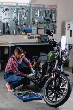 Tulumlu tamirci atölyedeki alet kutusunun yanında motosiklet kontrolü yapıyor.