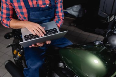 Atölyede motosiklet üzerinde otururken bilgisayar kullanan teknisyen görüntüsü