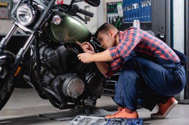 Tulumlu tamirci elinde el feneri tutarken motosiklet kontrolü yapıyor.