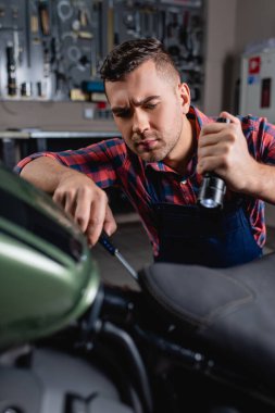 mechanic using flashlight and screwdriver during diagnostics of motorbike clipart