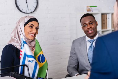 smiling african american and arabian business partners looking at interpreter on blurred foreground clipart