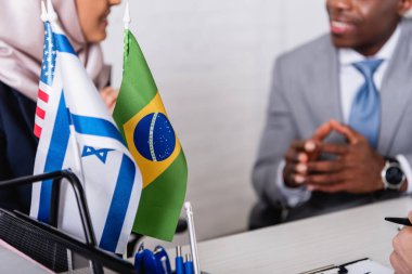 Arap ve Afro-Amerikan iş ortaklarının yakınlarındaki Brezilya, Amerika ve Uae bayraklarının seçici odak noktası bulanık arka plan, kırpık görüş