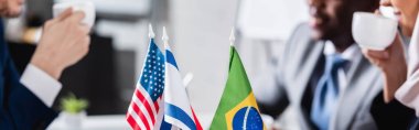 Amerikan, Brezilyalı ve ABD bayraklarının seçici odak noktası çok kültürlü iş adamlarının yanında bulanık arka planda kahve içmeleri, kısmi manzara, afiş