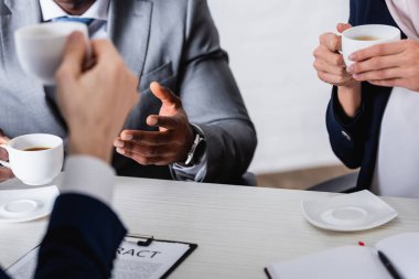 Kahve molası sırasında bardakları tutan çok ırklı iş ortaklarının seçici odak noktası, bulanık önplan, kırpık görüş