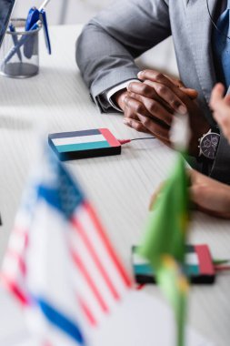 Afro-Amerikan iş adamının, elleri sımsıkı bağlı bir şekilde dijital çevirmenin yanında oturduğu, uae bayrağı amblemi ile bulanık ön plan