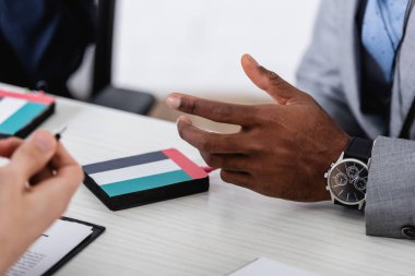 cropped view of african american businessman gesturing near interpreter and digital translator with uae flag, blurred foreground clipart