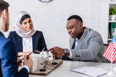 Mutlu Afro-Amerikan iş adamı, çok ırklı ortakların yakınında rüzgar türbinleri bulunan alternatif enerji santrali modelini işaret ediyor.