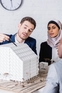 Çevirmen, Arap ve Afro-Amerikan ortakların yakınında güneş pilleri bulunan bir inşaat modelini işaret ederek ön planı bulanıklaştırdı 
