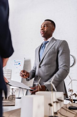 Afro-Amerikan işadamı elinde kalem, sözleşmenin yanında ve bulanık ön planda yeşil elektrik santrali tutuyor.
