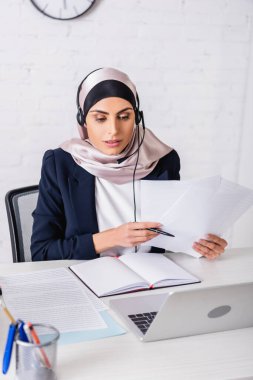 Boş defter ve dizüstü bilgisayarın yanında çalışan kulaklık içindeki Arapça çevirmen, bulanık önplan