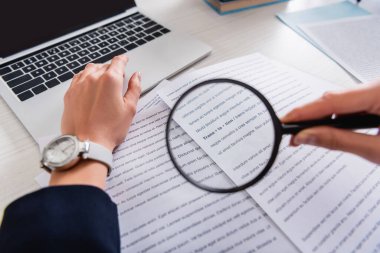 cropped view of translator holding magnifier glass near documents with english text, blurred foreground clipart