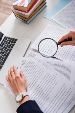 Dizüstü bilgisayar ve yabancı dillerin sözlükleri yakınındaki belgelerin üzerinde büyüteç tutan çevirmenin kısmi görünümü