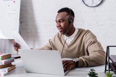 Gülümseyen Afro-Amerikan tercüman bulanık önplandaki dizüstü bilgisayar ve sözlükleri tercüme ediyor