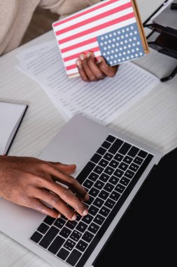 Kapağında ABD bayrağı olan sözlüğü tutarken dizüstü bilgisayarda yazan Afrika kökenli Amerikalı çevirmen görüntüsü