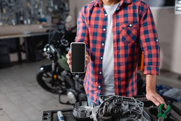 motorsiklet yedek parçalarının yanında boş ekranlı akıllı telefonu tutan mekanik görüntüsü, bulanık arkaplan