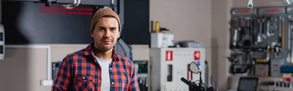 Young Mechanic Plaid Shirt Beanie Smiling Camera Workshop Banner — Stock Photo, Image