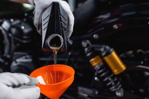 partial view of mechanic in gloves pouring engine oil from bottle into funnel