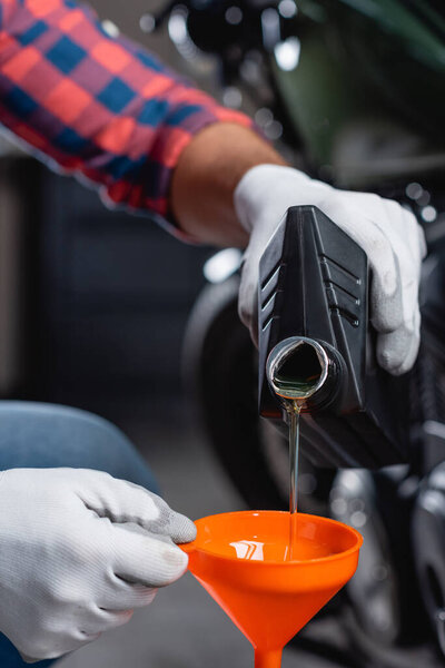 partial view of mechanic in gloves pouring motor oil from bottle into funnel