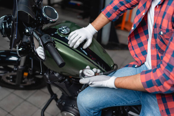 cropped view of technician in gloves measuring air pressure in tire of motorbike with manometer