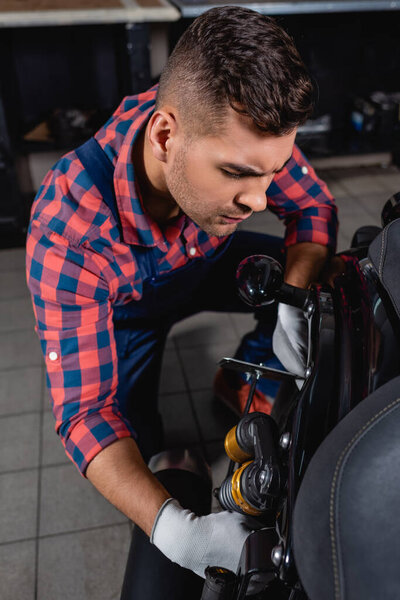 technician in plaid shirt examining shock absorber of motorbike in workshop
