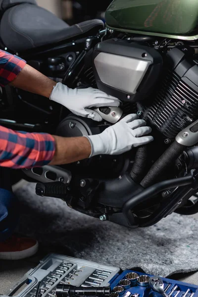 作業場の工具箱の近くのバイクをチェックする手袋の修理工のクロップドビュー — ストック写真