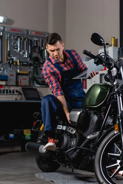 Ремонтник Комбінезоні Перевіряє Мотоцикл Тримаючи Ноутбук — стокове фото