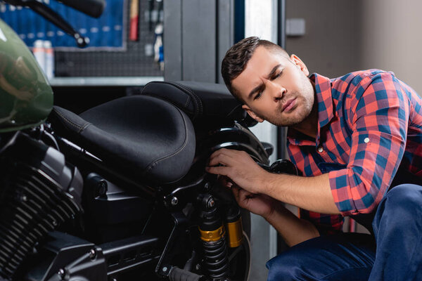 repairman in plaid shirt making diagnostics of motorbike in workshop