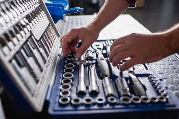 partial view of mechanic choosing instrument in toolbox on blurred foreground