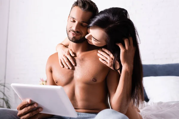 黑发女人抱在床上用平板电脑引诱笑脸的男人 — 图库照片