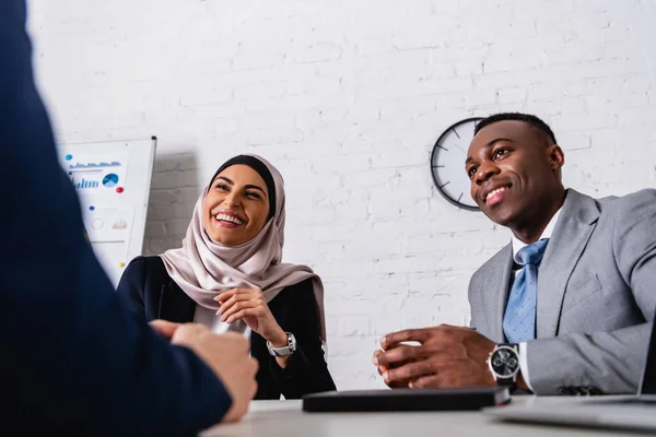 excited arabian businesswoman laughing during meeting with african american business partner and interpreter, blurred foreground