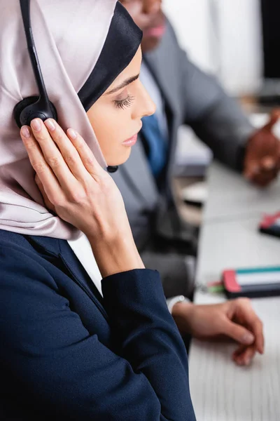 アフリカ系アメリカ人ビジネスパートナーの近くにヘッドセットに触れるアラビア人のビジネス女性 — ストック写真