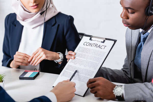 cropped view of interpreter pointing with pen at contract near african american and arabian business partners