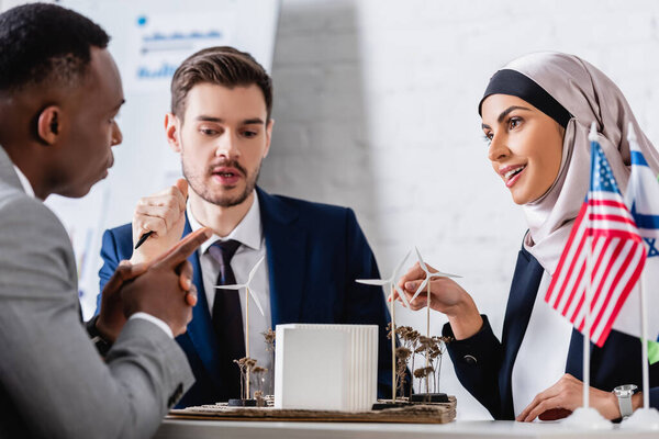 arabian businesswoman pointing at alternative power station near multiethnic business partners, blurred foreground