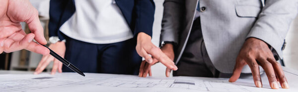 обрезанный взгляд многонациональных деловых партнеров, указывающих на чертеж во время встречи, баннер