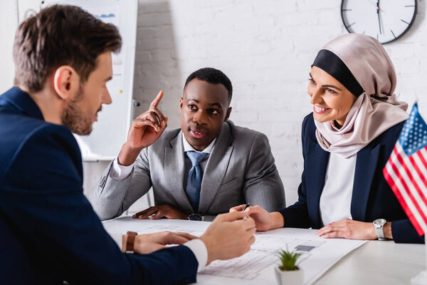 cheerful arabian businesswoman looking at interpreter near african american businessman showing idea gesture