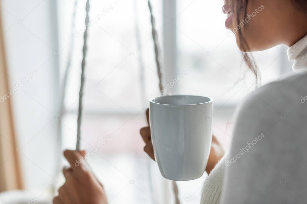 cropped view of african american woman holding cup of warm tea at home, blurred foreground