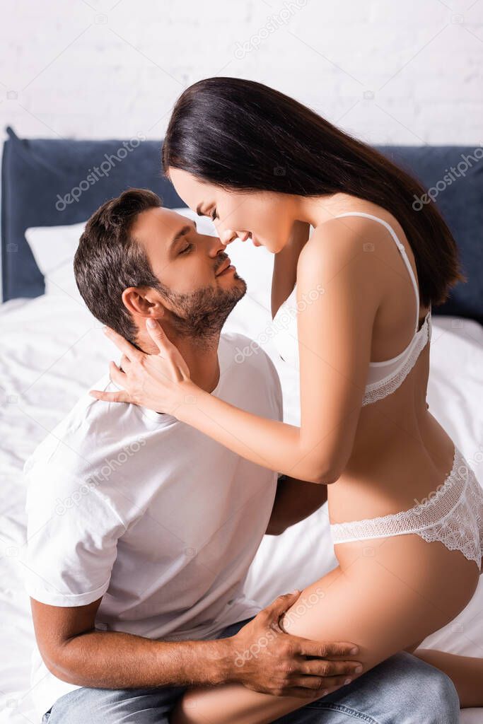 seductive young woman in lingerie hugging man in t-shirt and jeans on bed on blurred background