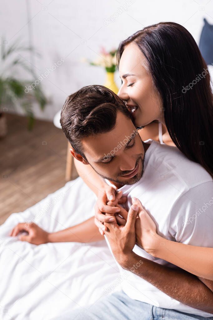 seductive brunette woman biting man in bedroom on blurred background