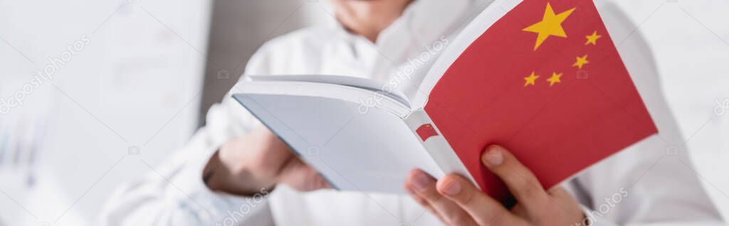 cropped view of interpreter holding chinese dictionary in translation agency, blurred background, banner