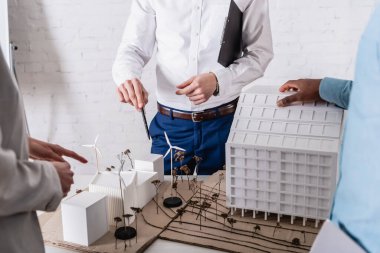 partial view of business partners pointing at model of clean energy station near african american businessman, blurred foreground clipart