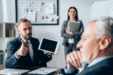 Dijital tabletli bir işadamı, bulanık önplanda gülümseyen bir iş arkadaşı ve yatırımcı olduğunu gösteriyor. 