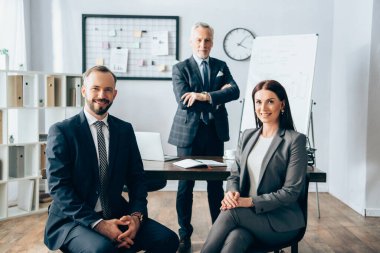 Gülümseyen iş ortakları arka planda olgun meslektaşlarının yanında kameraya bakıyorlar. 