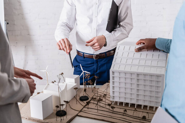 partial view of business partners pointing at model of clean energy station near african american businessman, blurred foreground