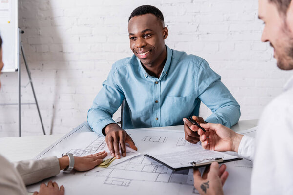 interpreter holding contract and pen while woman giving bribe to happy african american businessman, blurred foreground