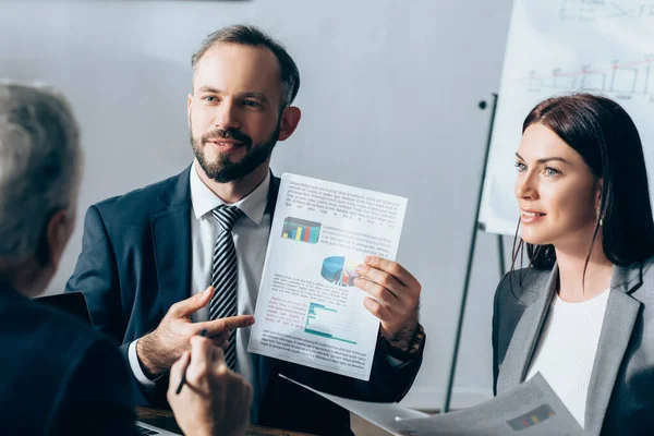 Gülümseyen işadamı, meslektaşının yakınındaki belgeye işaret ediyor ve bulanık önplan üzerine danışmanlık yapıyor. 