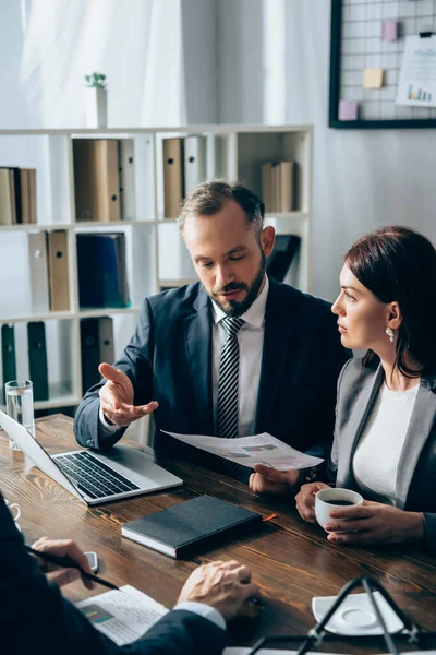 Businessman Holding Paper Pointing Investor Blurred Foreground Laptop Colleague Coffee — Stock Photo, Image