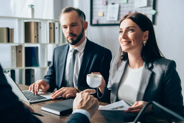 Mujer Negocios Sonriente Sosteniendo Taza Cerca Colega Utilizando Ordenador Portátil — Foto de Stock